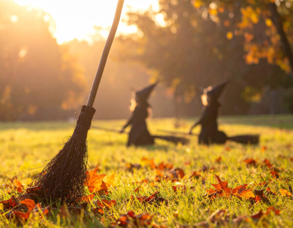 Två barn hoppar på häxkvastar på en äng med höstlöv